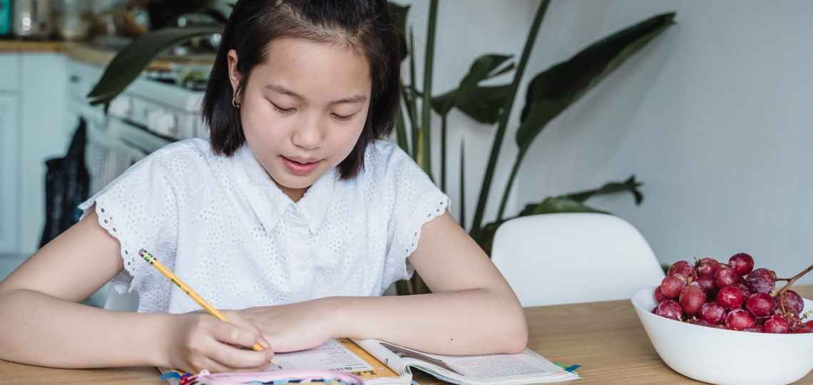 a girl in white top writing on a notebook