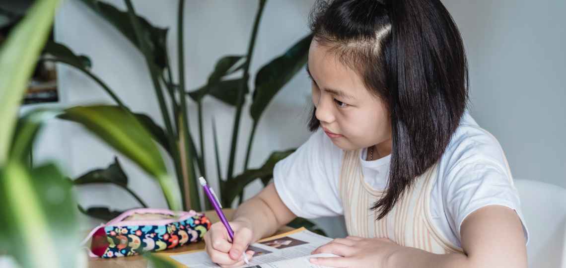 a young girl in white shirt studying on a table