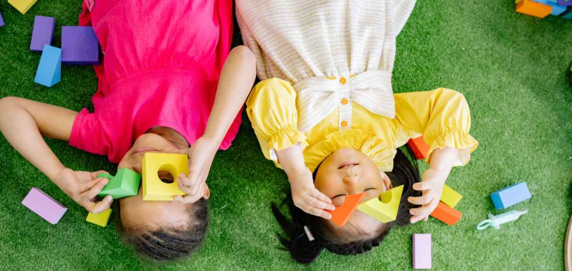 girls lying down on green carpet playing with wooden blocks