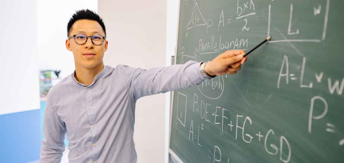 man wearing eyeglasses pointing at the blackboard