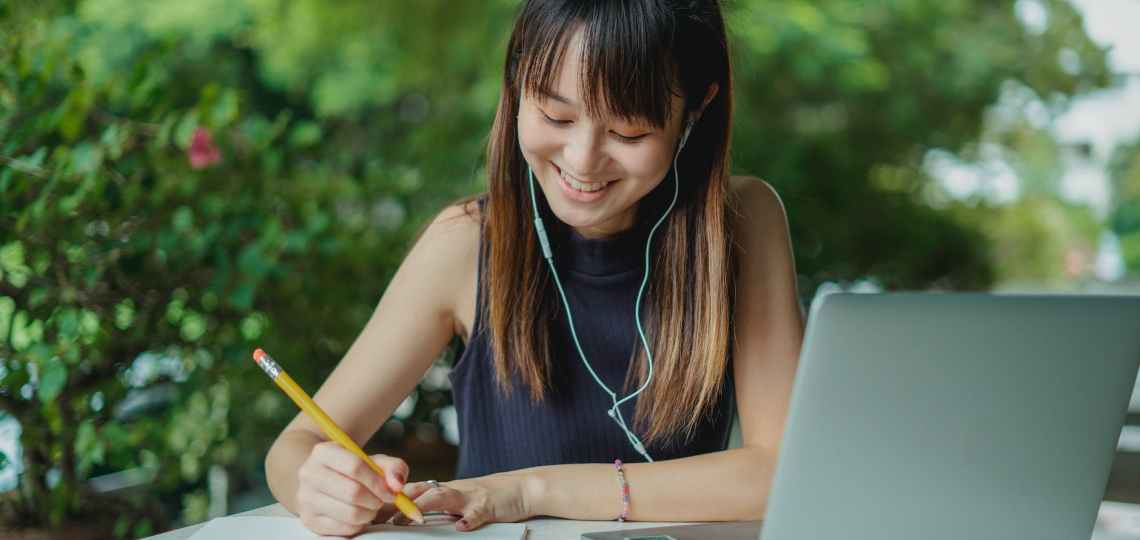 happy young asian student doing homework and listening to music with earphones