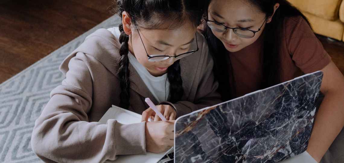 girls wearing eyeglasses having conversation while writing on a notebook