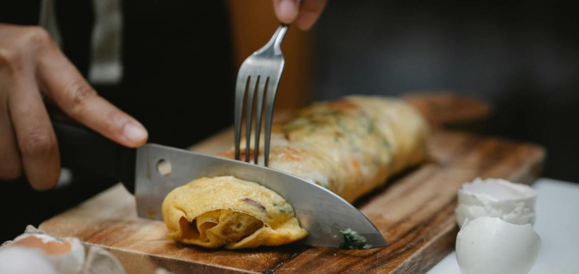 crop unrecognizable chef cutting egg roll in kitchen