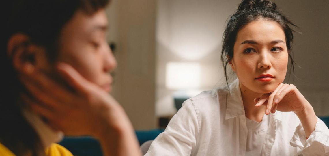 thoughtful young ethnic women having conversation at table at home