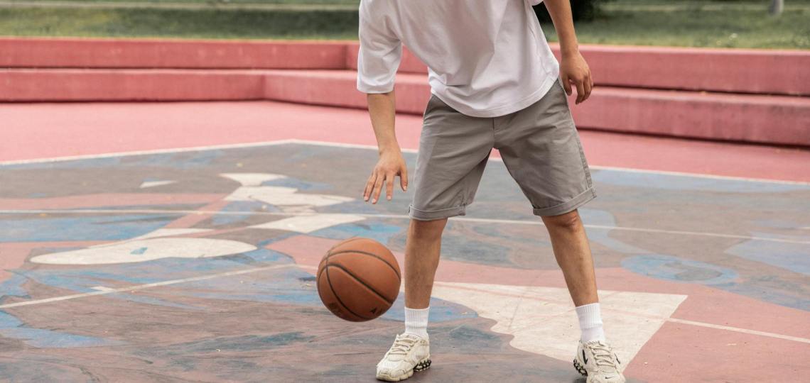 crop active asian sportsman dribbling basketball ball on court