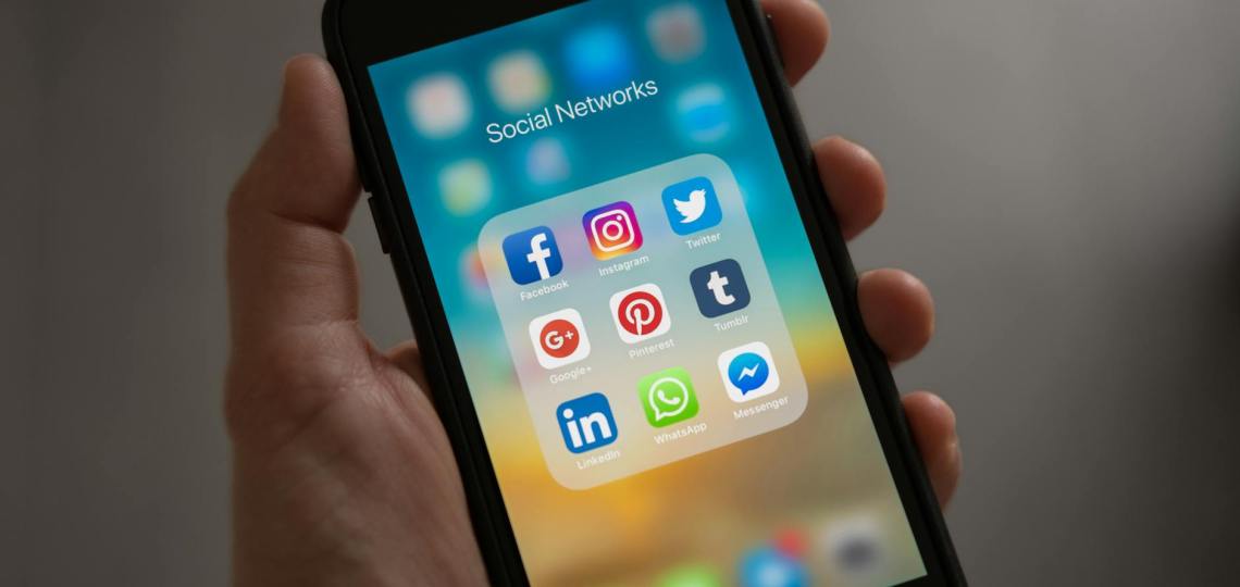 person holding iphone showing social networks folder